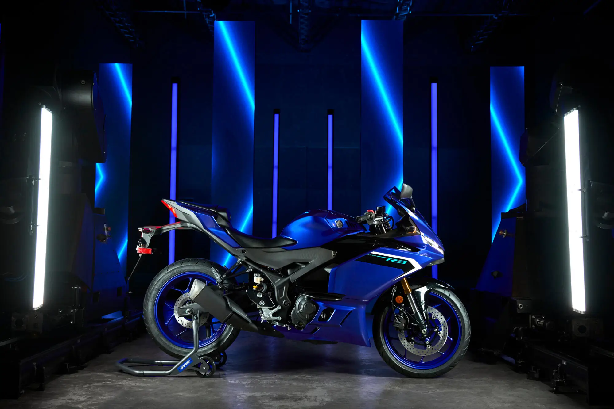 2025-Yamaha-YZF-R320-EU-Detail-001-03 Ein blaues Yamaha YZF-R320 Motorrad steht in einem futuristischen Raum mit blauer Beleuchtung.