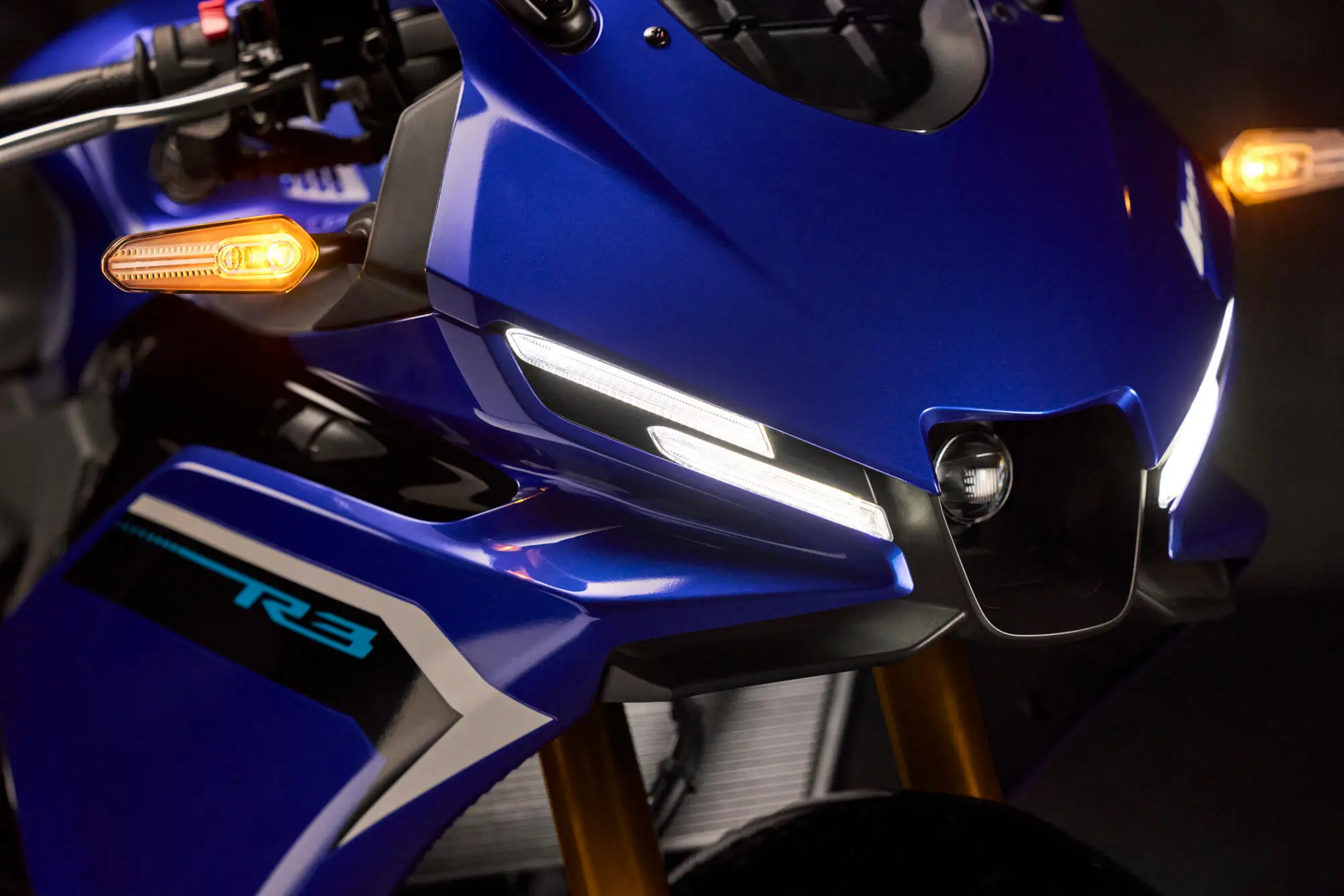 2025-Yamaha-YZF-R320-EU-Detail-002-03 Nahaufnahme der Front einer blauen Yamaha YZF-R320 mit leuchtenden Scheinwerfern.