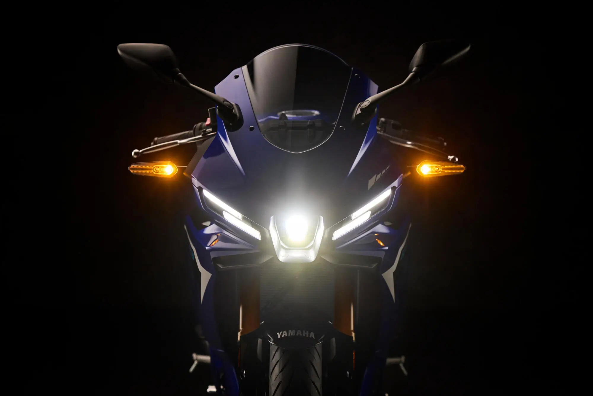 2025-Yamaha-YZF-R320-EU-Detail-003-03 Frontansicht eines 2025 Yamaha YZF-R320 Motorrads mit eingeschaltetem Scheinwerfer und Blinker.
