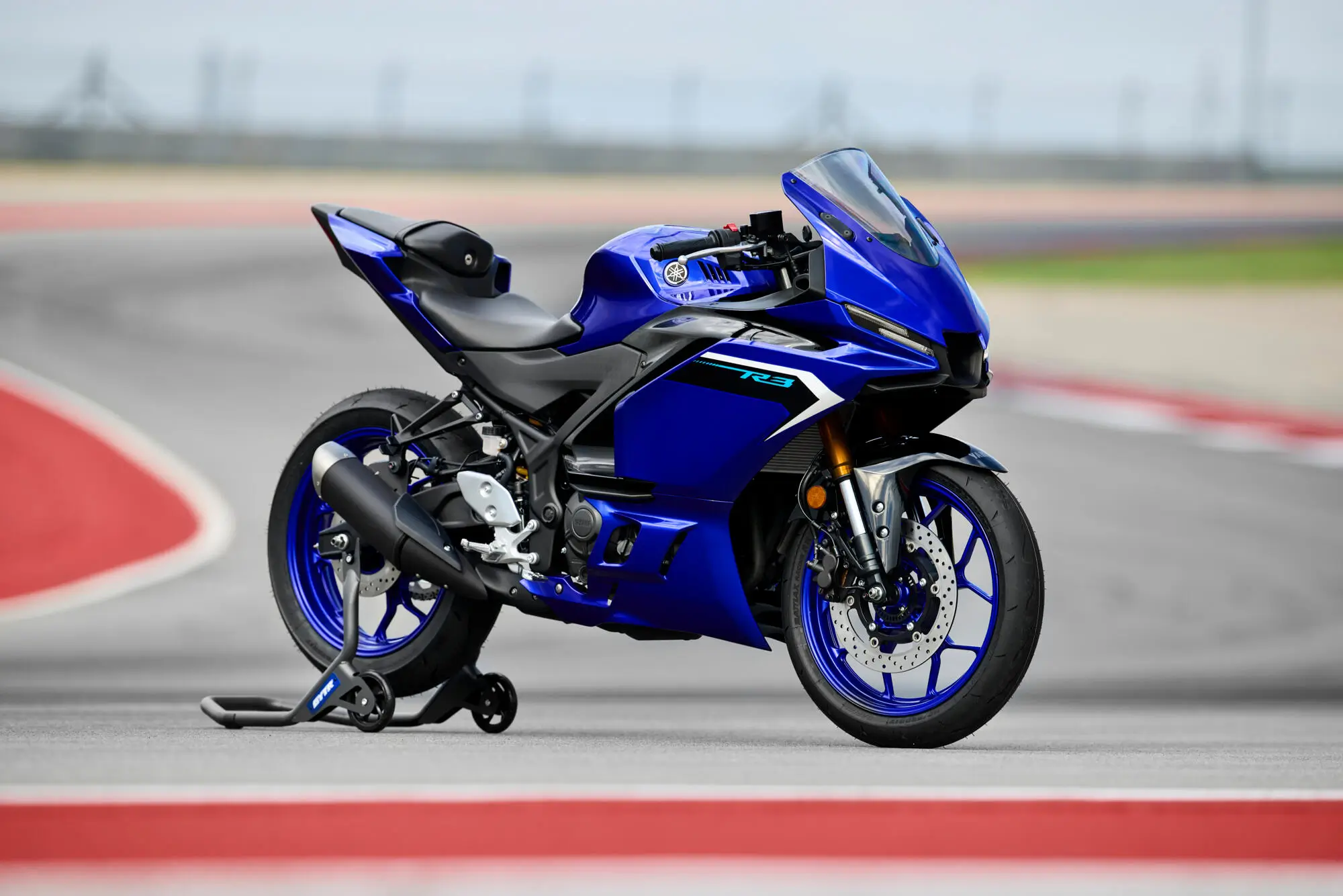 2025-Yamaha-YZF-R320-EU-Detail-004-03 Ein blaues Yamaha YZF-R3 Motorrad steht auf einer Rennstrecke.