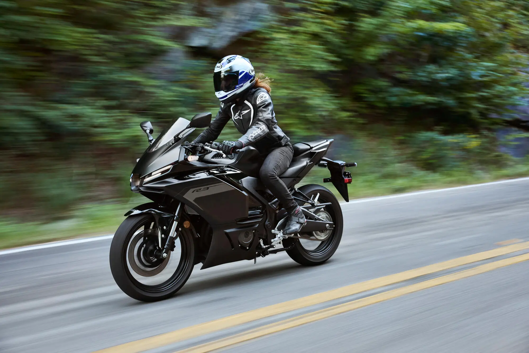 Eine Person fährt eine schwarze Yamaha YZF-R3 auf einer Landstraße.