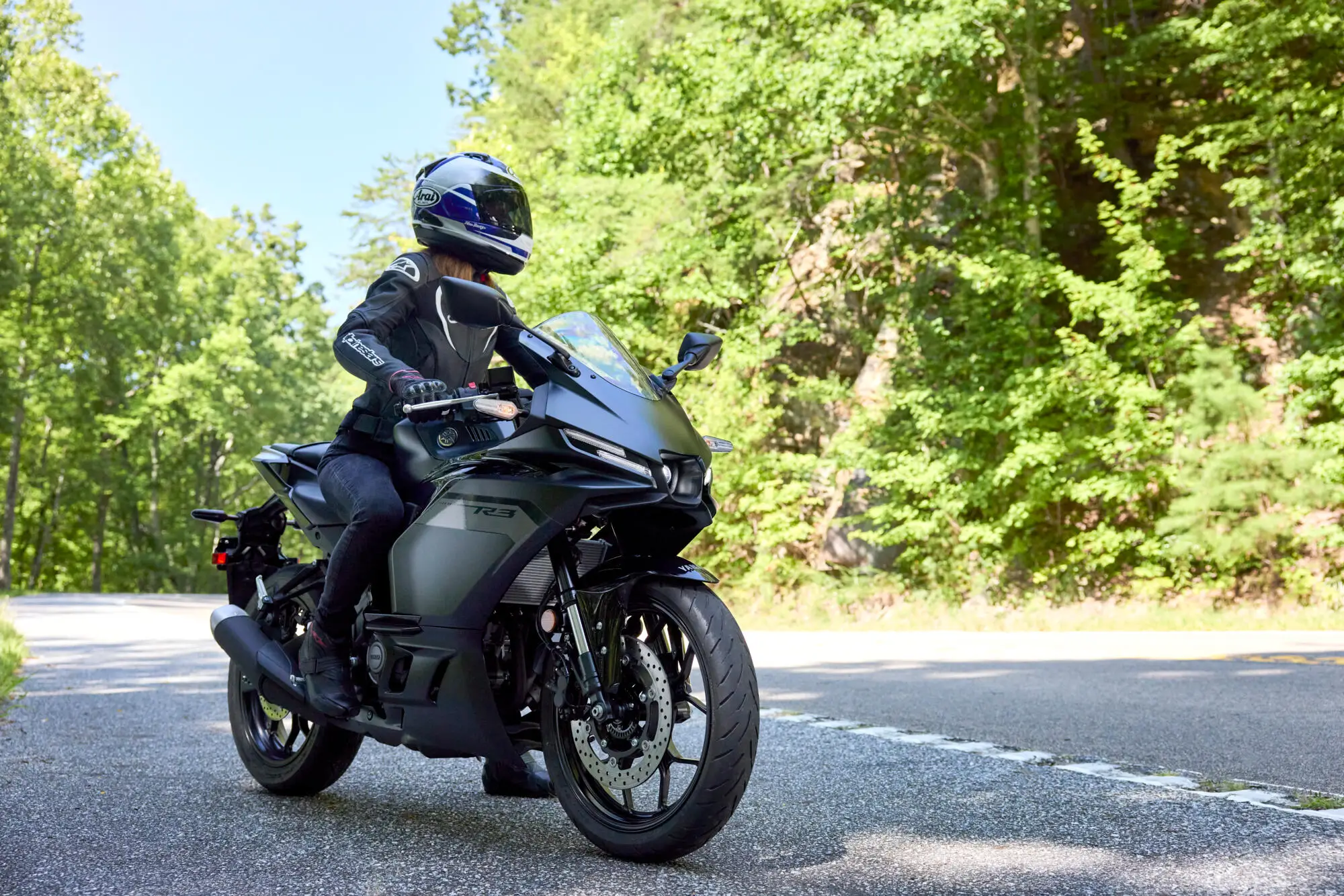 Eine Person fährt eine schwarze Yamaha YZF-R3 auf einer kurvigen Landstraße.