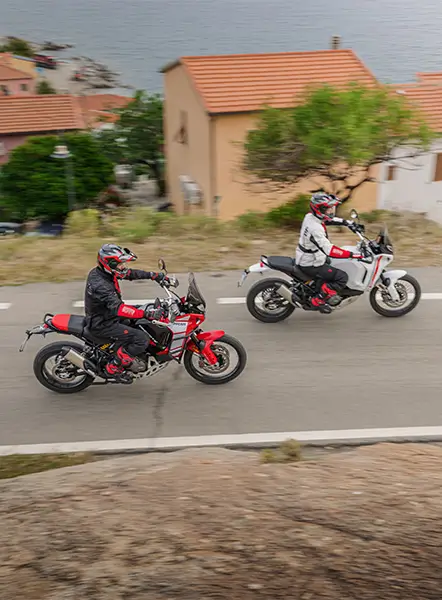 Zwei Personen fahren auf Ducati DesertX Motorrädern auf einer Straße.