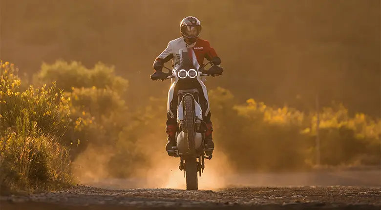 Ein Motorradfahrer fährt eine Ducati DesertX auf einer staubigen Straße bei Sonnenuntergang.