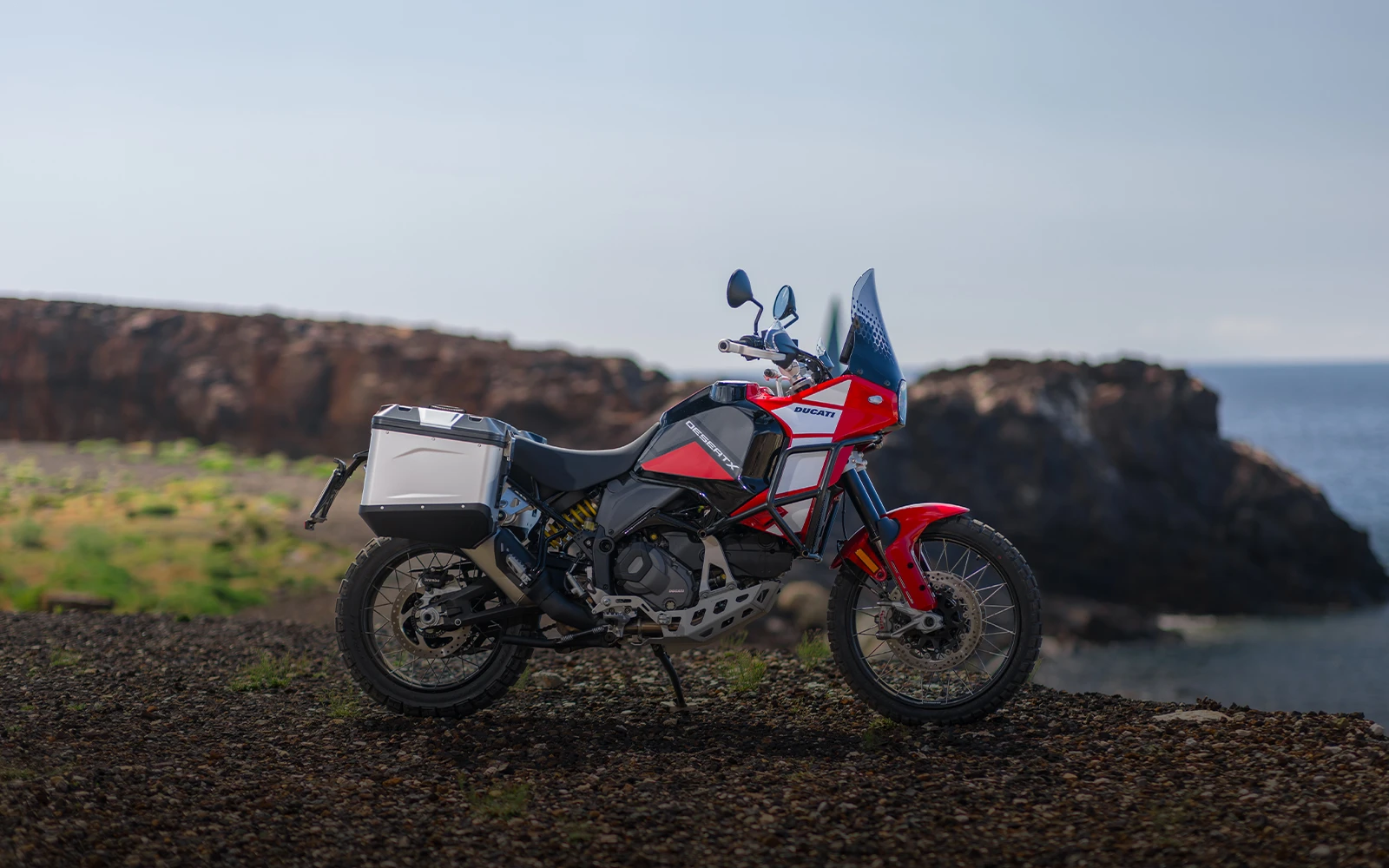 Ducati DesertX Motorrad steht auf einer felsigen Küstenlandschaft.