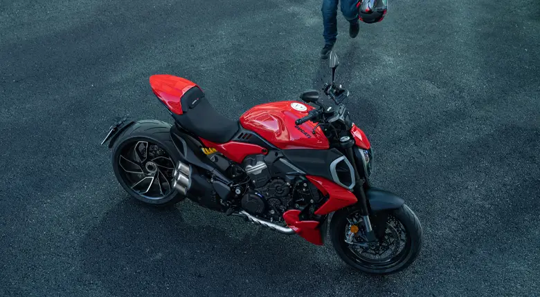 Ein rotes Ducati Diavel V4 Motorrad auf einer Straße, mit einer Person, die einen Helm hält.