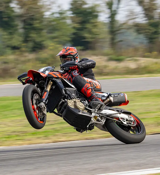 Ducati-Hypermotard-Mono-DWP24-Elettronica-carousel-imgtxt-677x740-03 Ein Motorradfahrer macht einen Wheelie mit einer Ducati Hypermotard auf einer Rennstrecke.