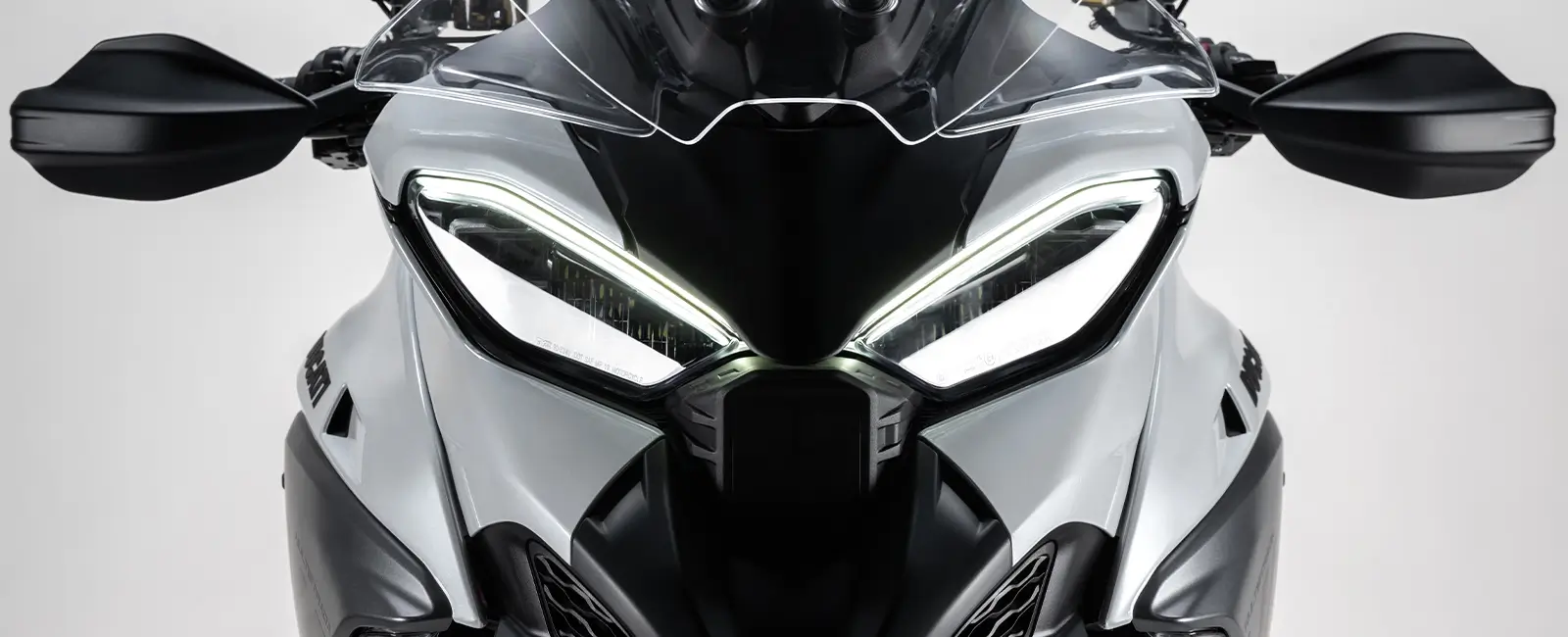 Ducati-MY25-Multistrada-V4-design-carousel-hero-link-1600x650-01 Frontansicht einer Ducati Multistrada V4 mit markanten LED-Scheinwerfern.