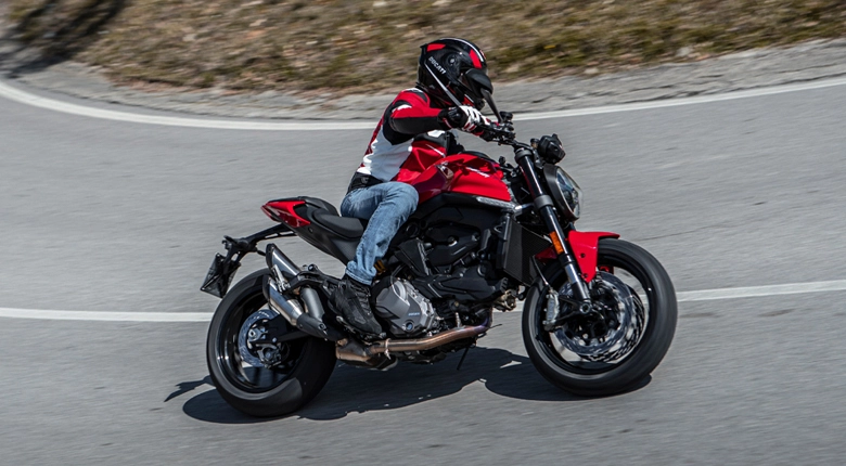 Ein Motorradfahrer auf einer Ducati Monster MY24 fährt in einer Kurve.
