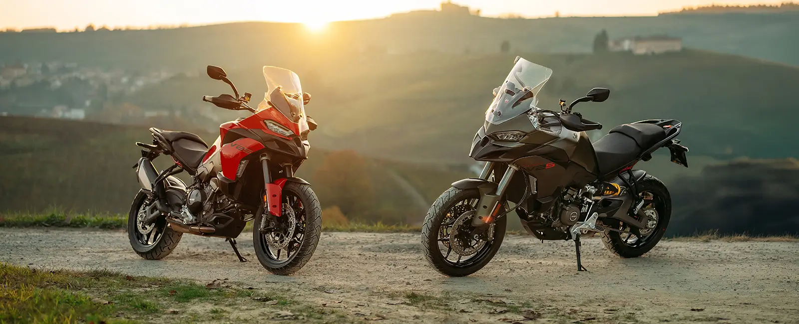 Ducati-Multistrada-V2-DWP25-overview-carousel-hero-link-1600x650-01 Zwei Ducati Multistrada V2 Motorräder stehen bei Sonnenuntergang auf einem Feldweg.