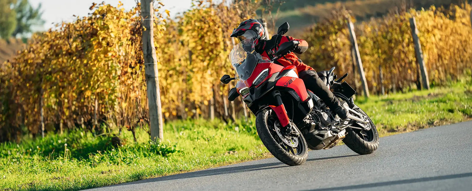 Ducati-Multistrada-V2-DWP25-overview-carousel-hero-link-1600x650-02 Ein Motorradfahrer fährt eine rote Ducati Multistrada V2 auf einer Landstraße.
