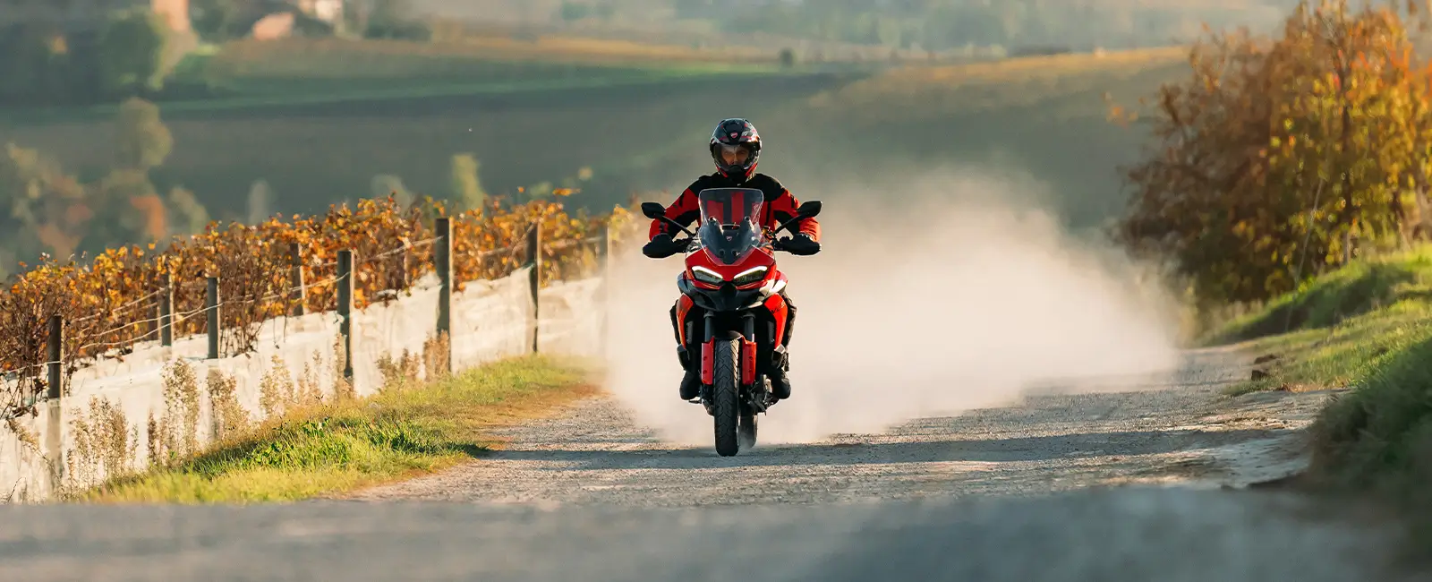 Ducati-Multistrada-V2-DWP25-overview-carousel-hero-link-1600x650-04 Ein Motorradfahrer fährt eine Ducati Multistrada V2 auf einer ländlichen Straße entlang.