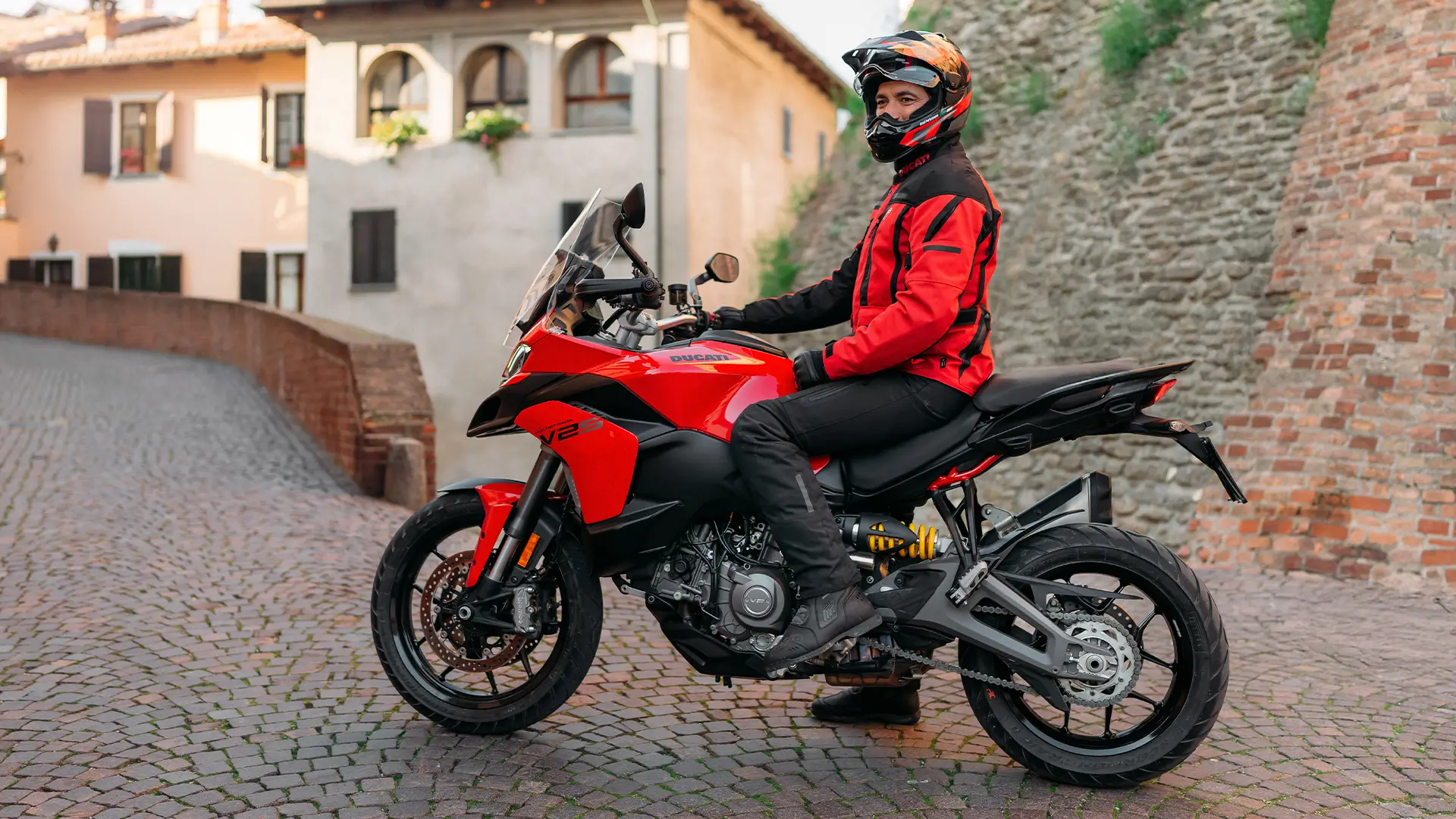 Eine Person sitzt auf einer Ducati Multistrada V2 in einer gepflasterten Altstadtumgebung.