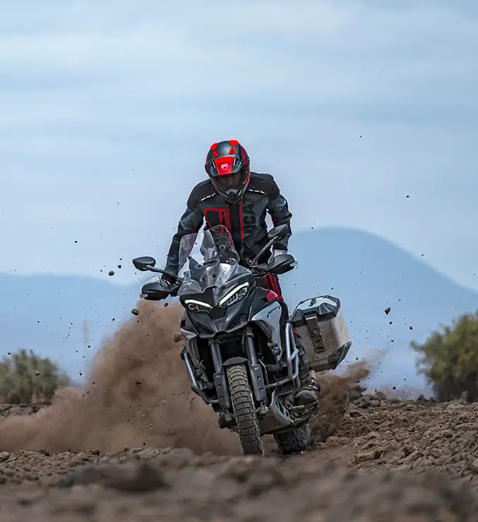 Ducati-Multistrada-V4-Rally-MY23-tech-spec-carousel-imgtxt-03-677x740 Fahrer auf einer Ducati Multistrada V4 Rally fährt durch schlammiges Gelände.