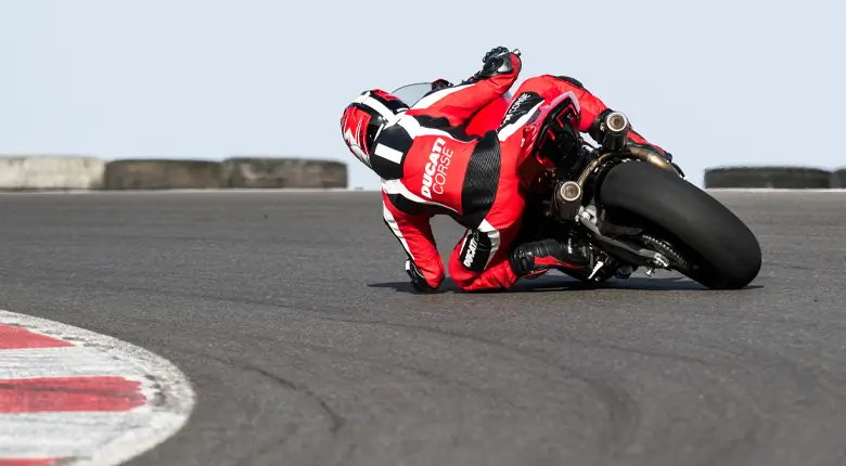 Ducati-Panigale-V2-V2S-Overview-mosaic-gallery-780x430-06 Ein Motorradfahrer in roter Schutzkleidung fährt eine Ducati Panigale V2 in Schräglage auf einer Rennstrecke.