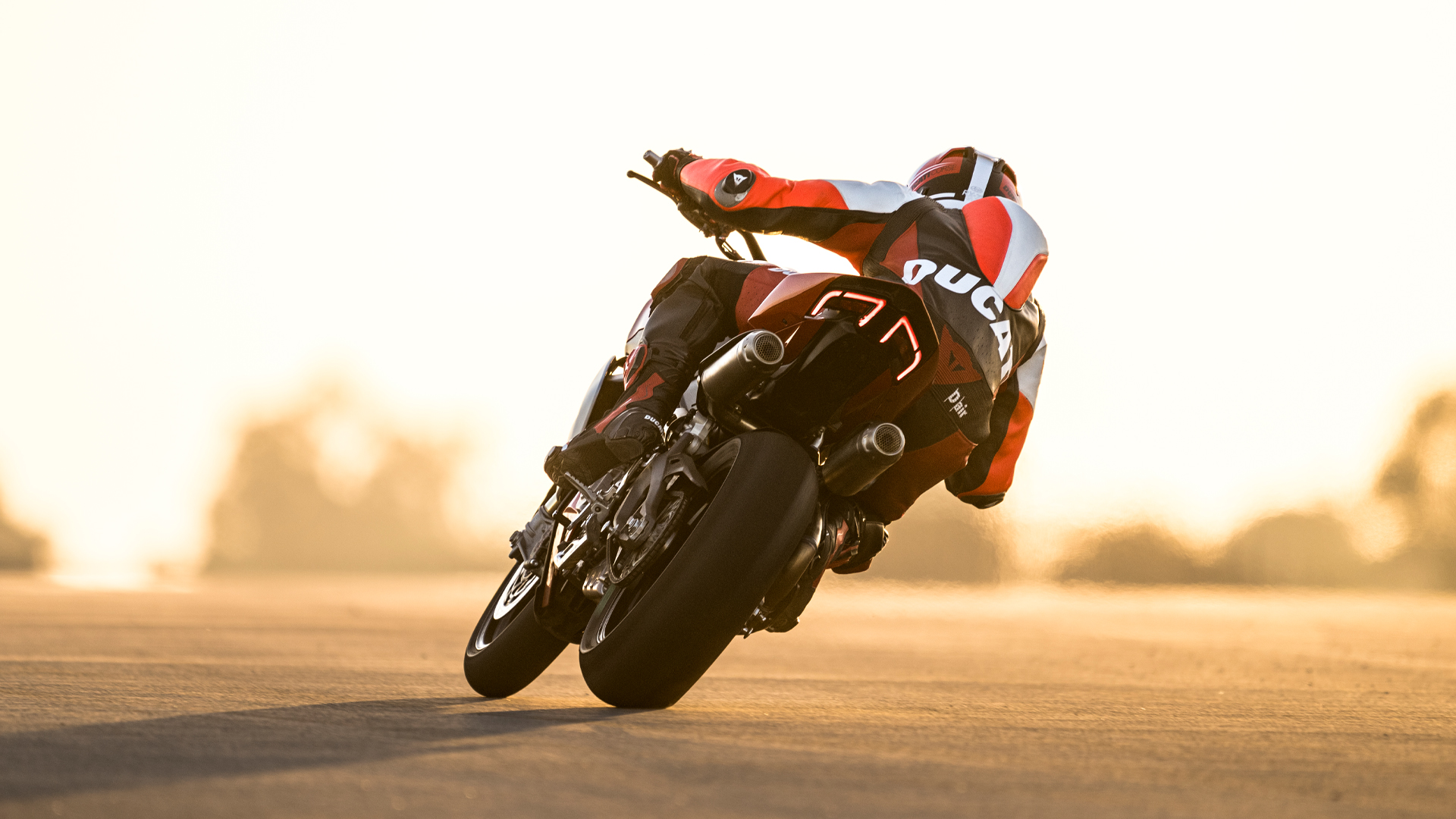 Ducati-Streetfighter-V2-V2S-overview-mosaic-gallery-1920x1080-06 Ein Motorradfahrer auf einer Ducati Streetfighter V2 fährt in eine Kurve bei Sonnenuntergang.