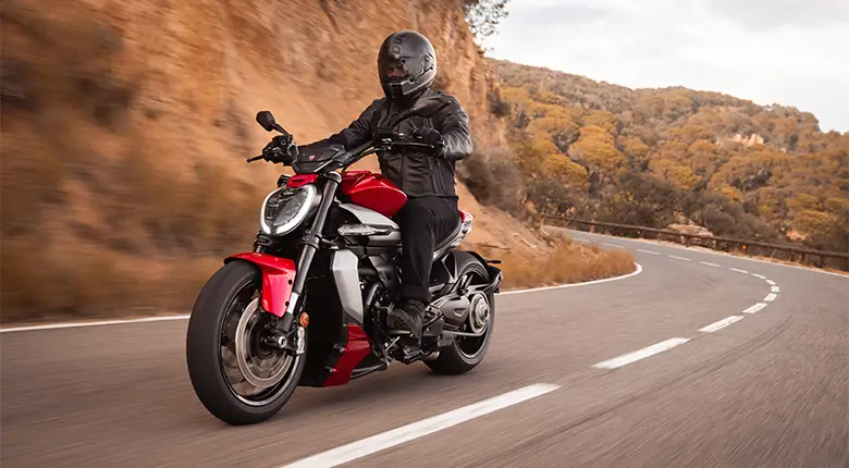Ein Motorradfahrer fährt eine Ducati XDiavel V4 auf einer kurvigen Landstraße.