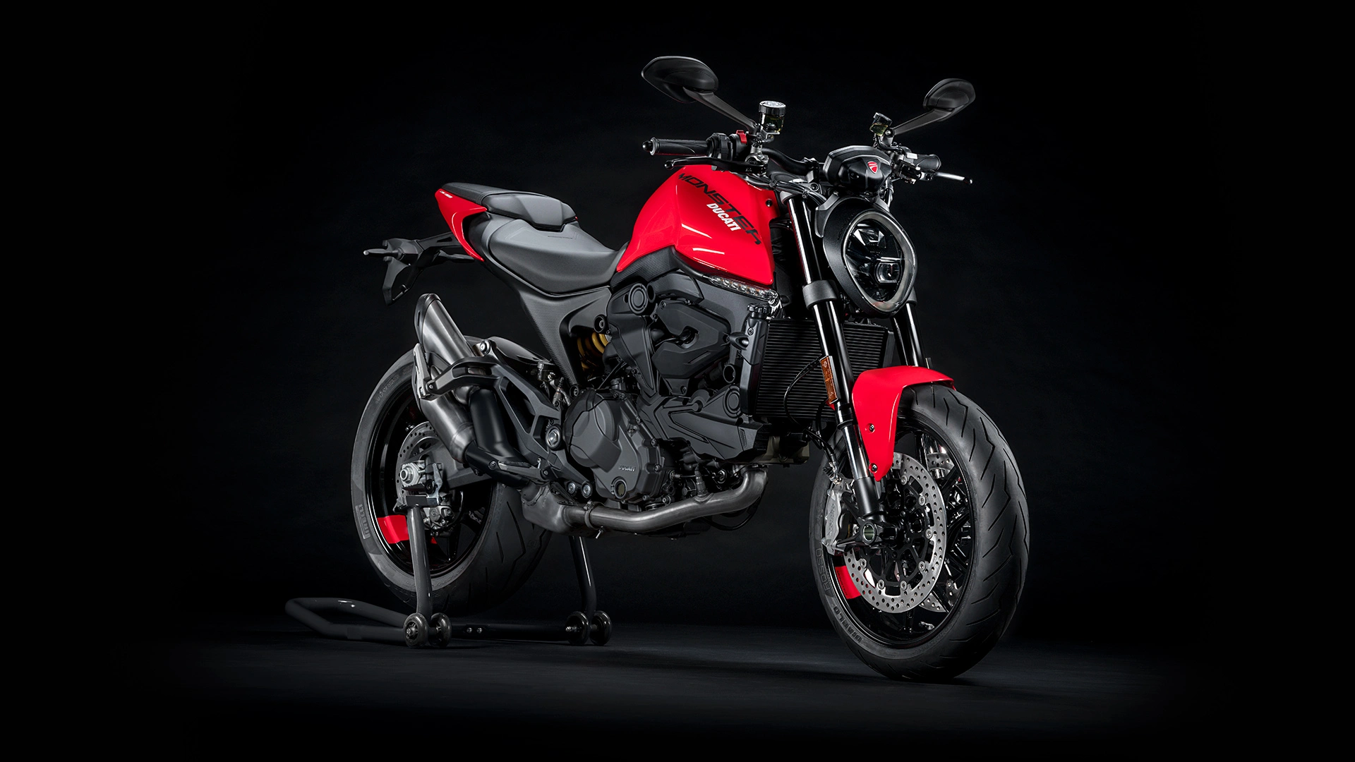 Ein rotes Ducati Monster Motorrad steht auf einem schwarzen Hintergrund.