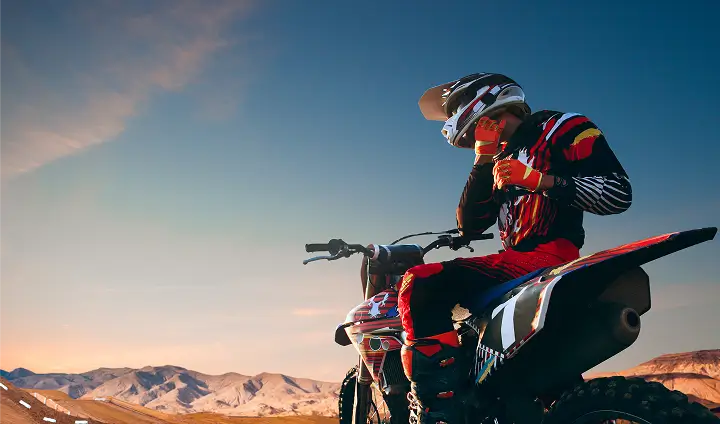 Ein Motorradfahrer in bunter Schutzkleidung sitzt auf einem Motorrad in einer Wüstenlandschaft.