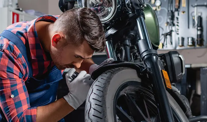 angebote_umbauten Ein Mechaniker inspiziert konzentriert das Vorderrad eines Motorrads in einer Werkstatt.