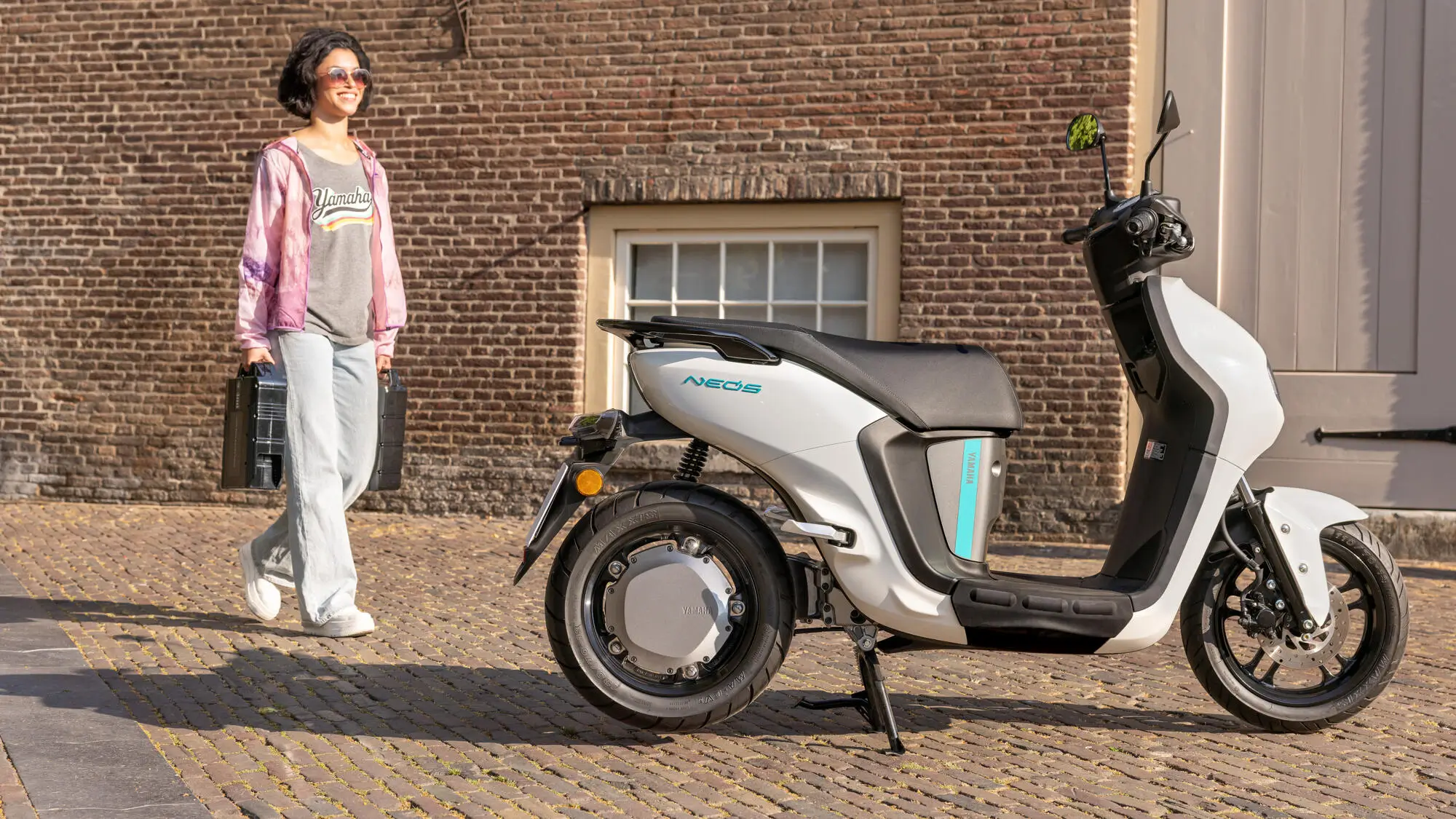 Eine Frau geht lächelnd neben einem weißen Yamaha Neos Roller.