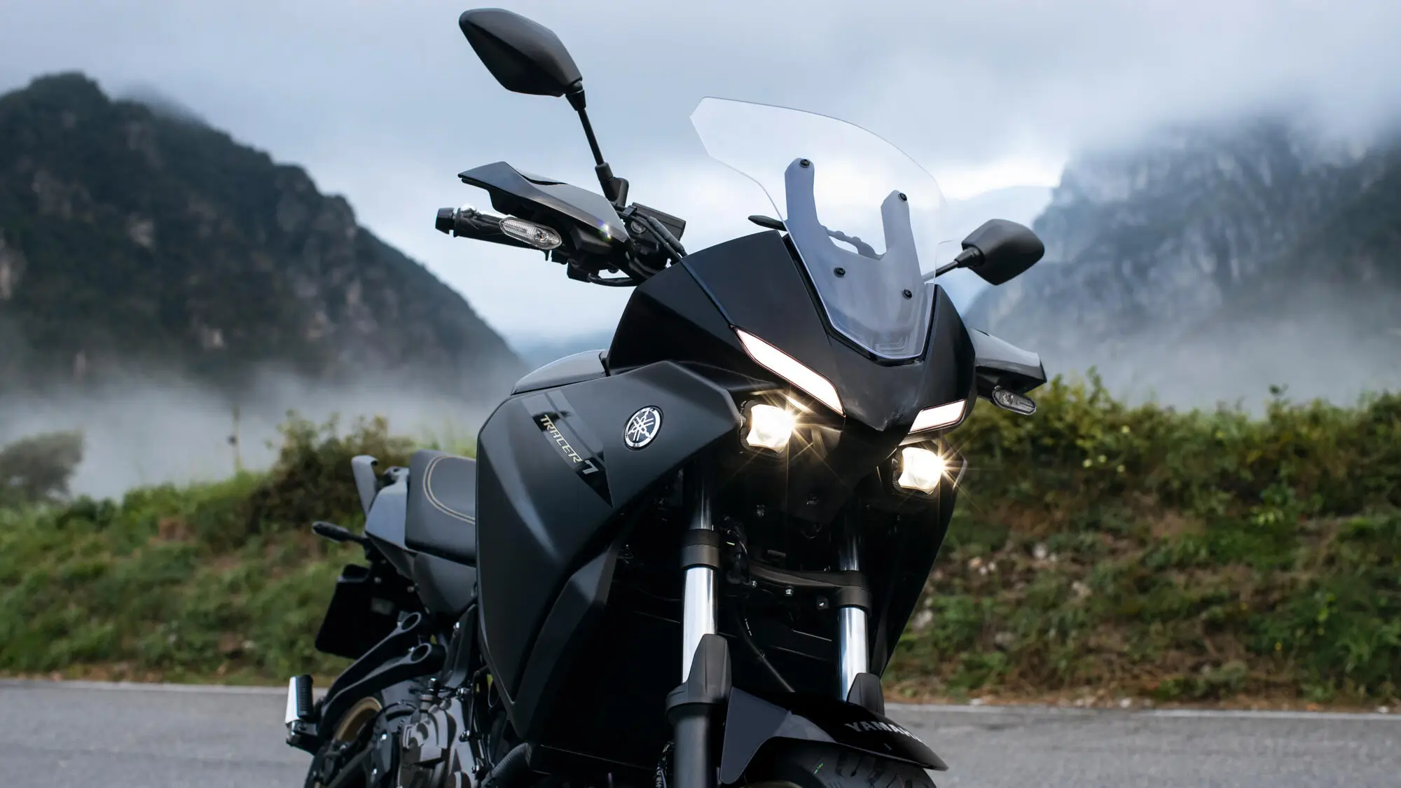 Ein schwarzes Yamaha MT-07 Motorrad steht auf einer Straße vor nebligen Bergen.