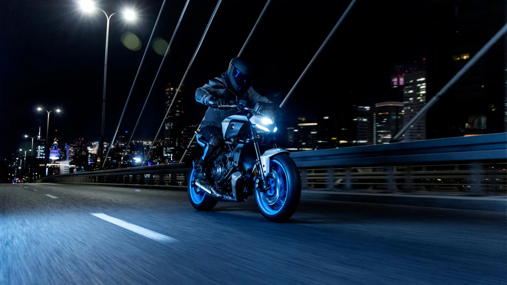 Ein Motorradfahrer fährt nachts auf einer Yamaha MT-07 über eine beleuchtete Brücke.