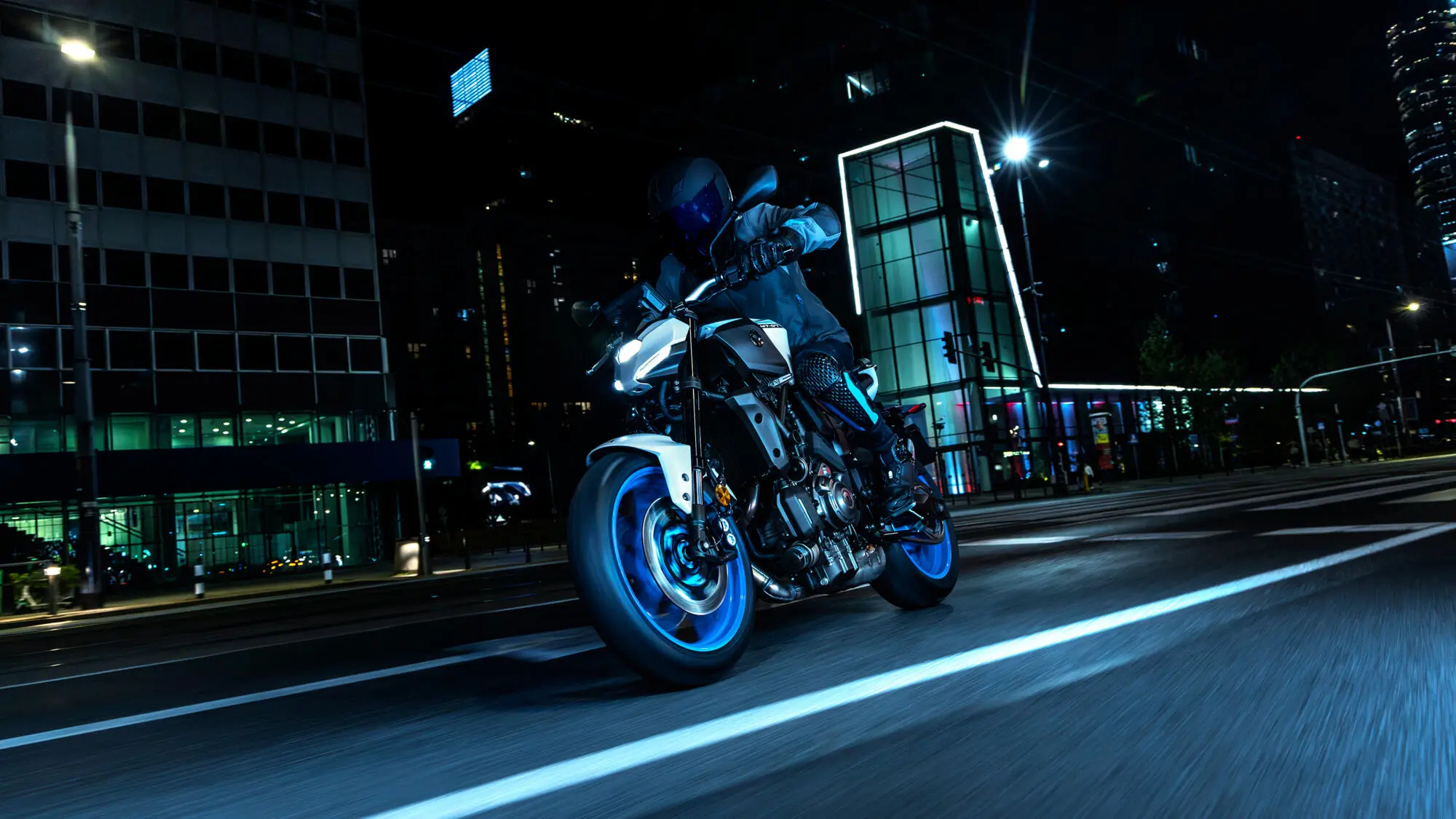 Ein Motorradfahrer fährt nachts auf einer Yamaha MT-07 durch eine beleuchtete Stadt.