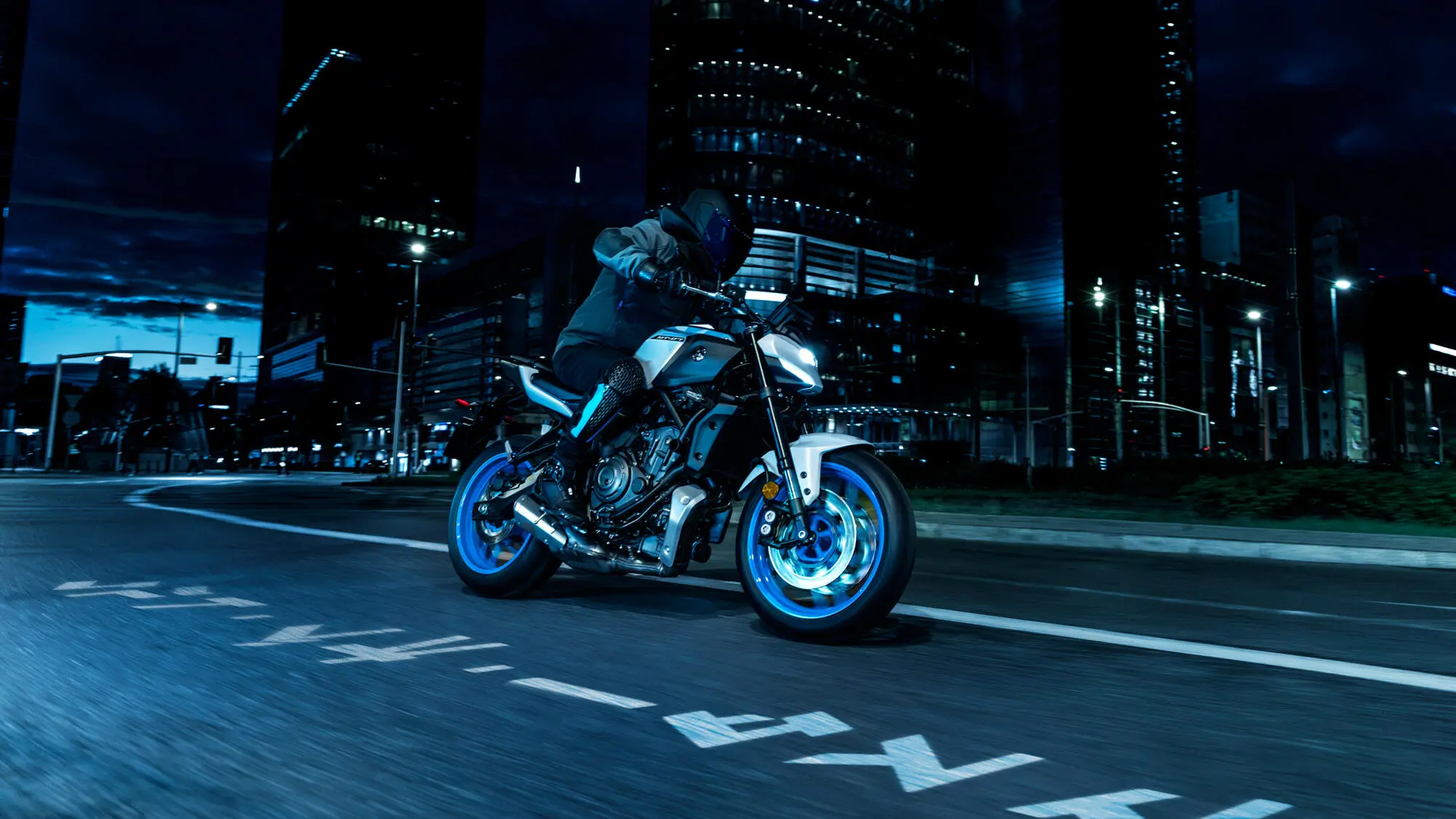 Ein Motorradfahrer fährt nachts auf einer Yamaha MT-07 durch eine beleuchtete Stadt.