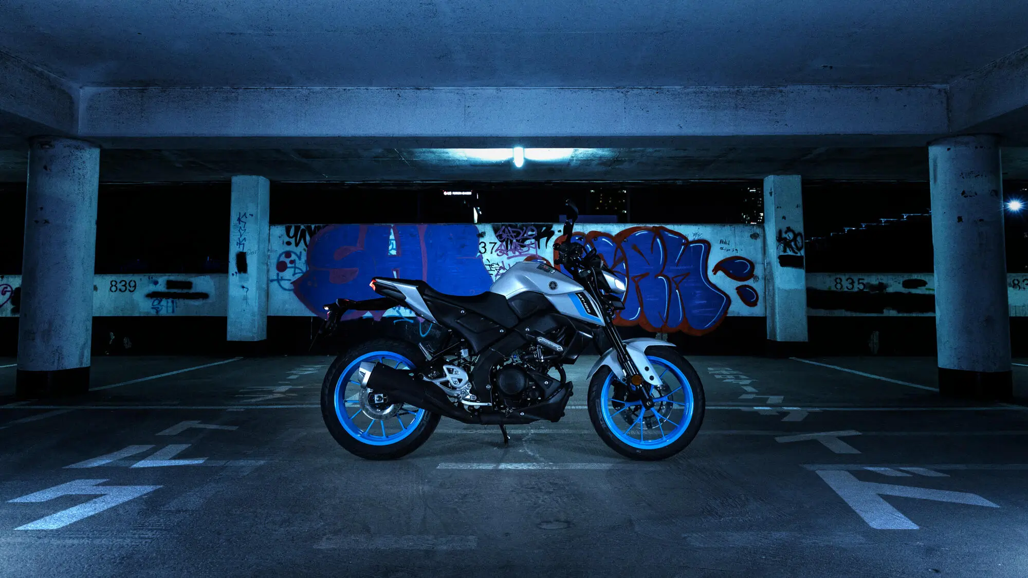 Yamaha MT-125A Motorrad in einem dunklen Parkhaus vor einer Wand mit Graffiti.