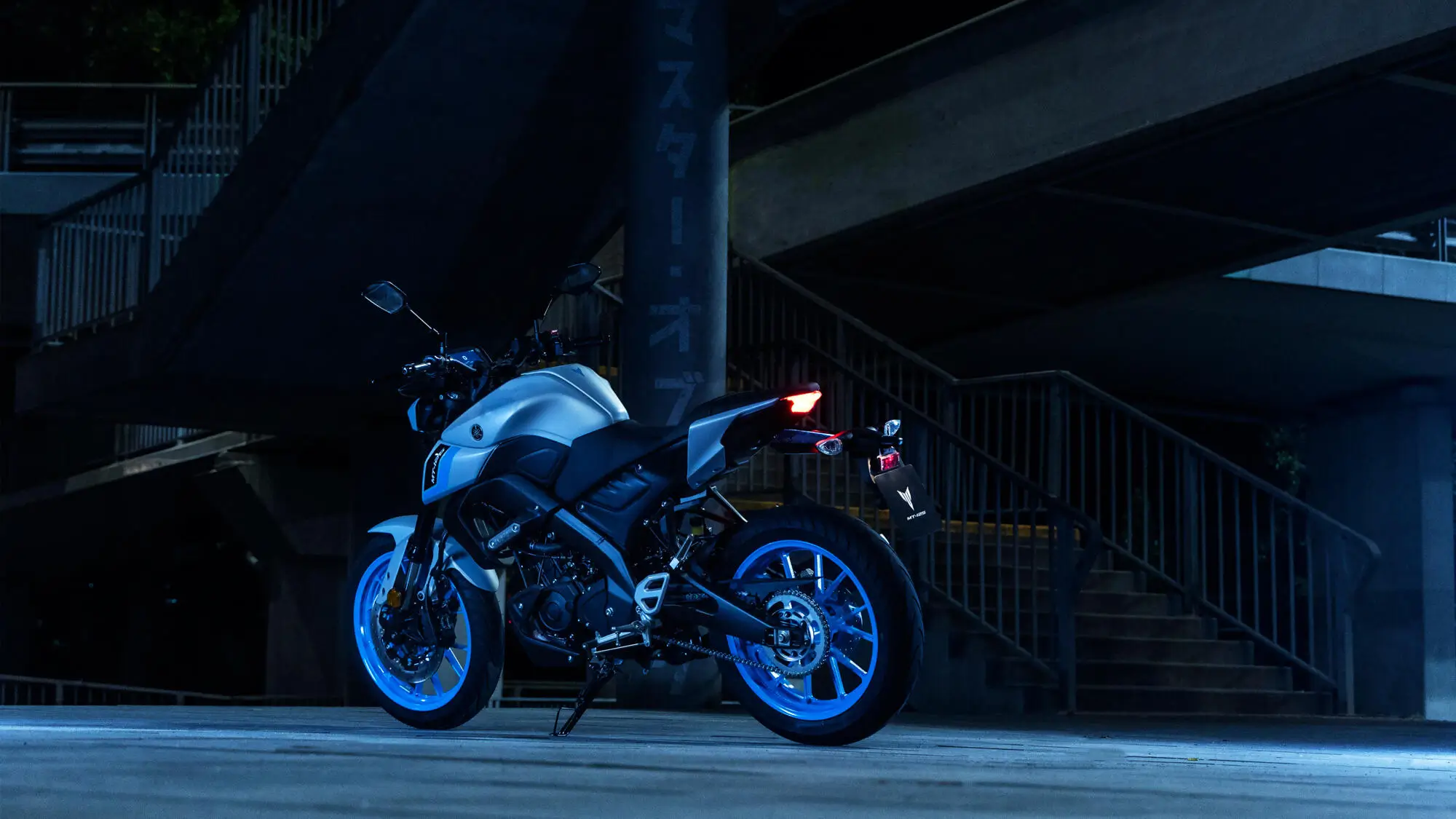 Ein silbernes Yamaha MT125A Motorrad steht nachts unter einer Treppe.