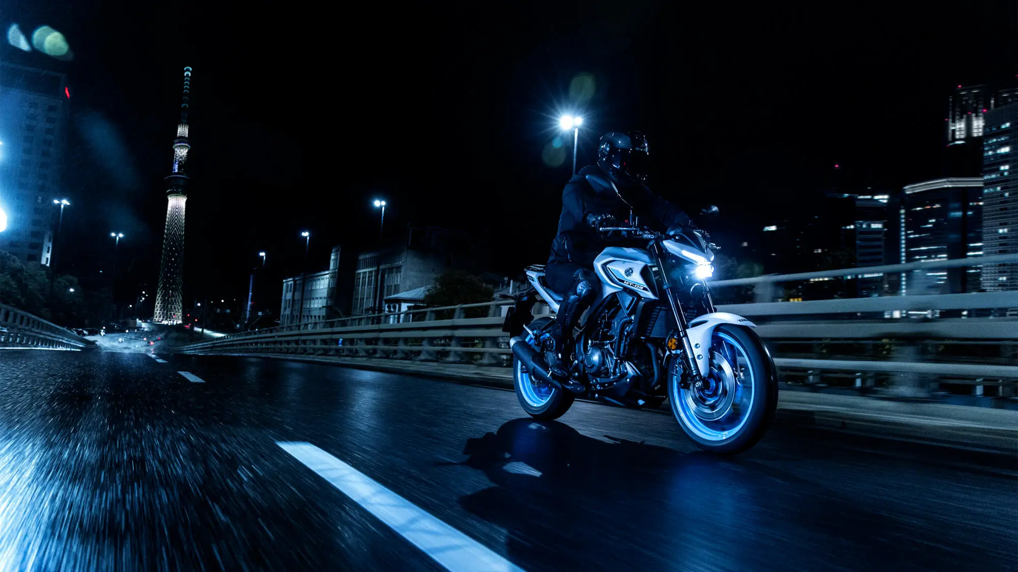 Motorradfahrer auf einer Yamaha MT320 fährt nachts durch eine beleuchtete Stadt.