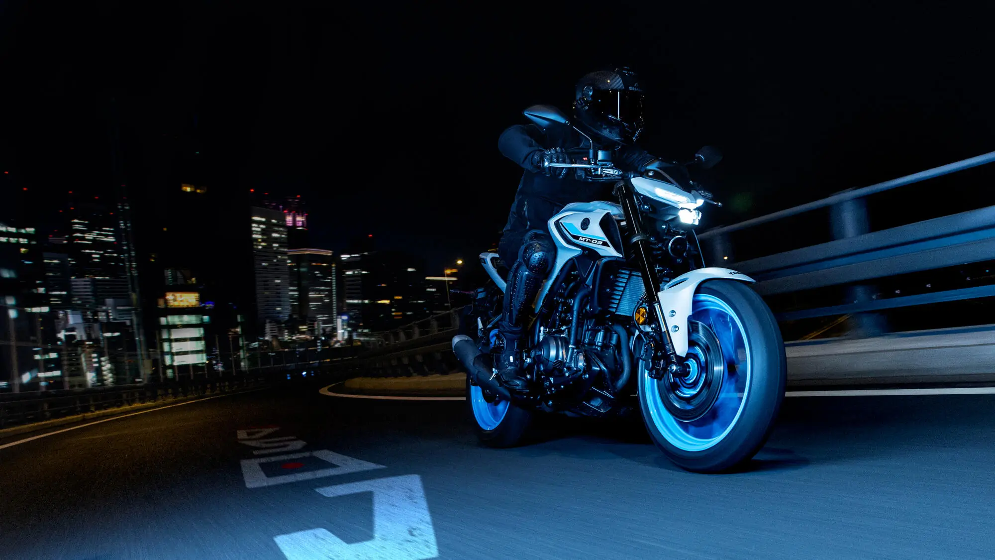 Ein Motorradfahrer fährt bei Nacht eine Yamaha MT-320 durch eine beleuchtete Stadt.