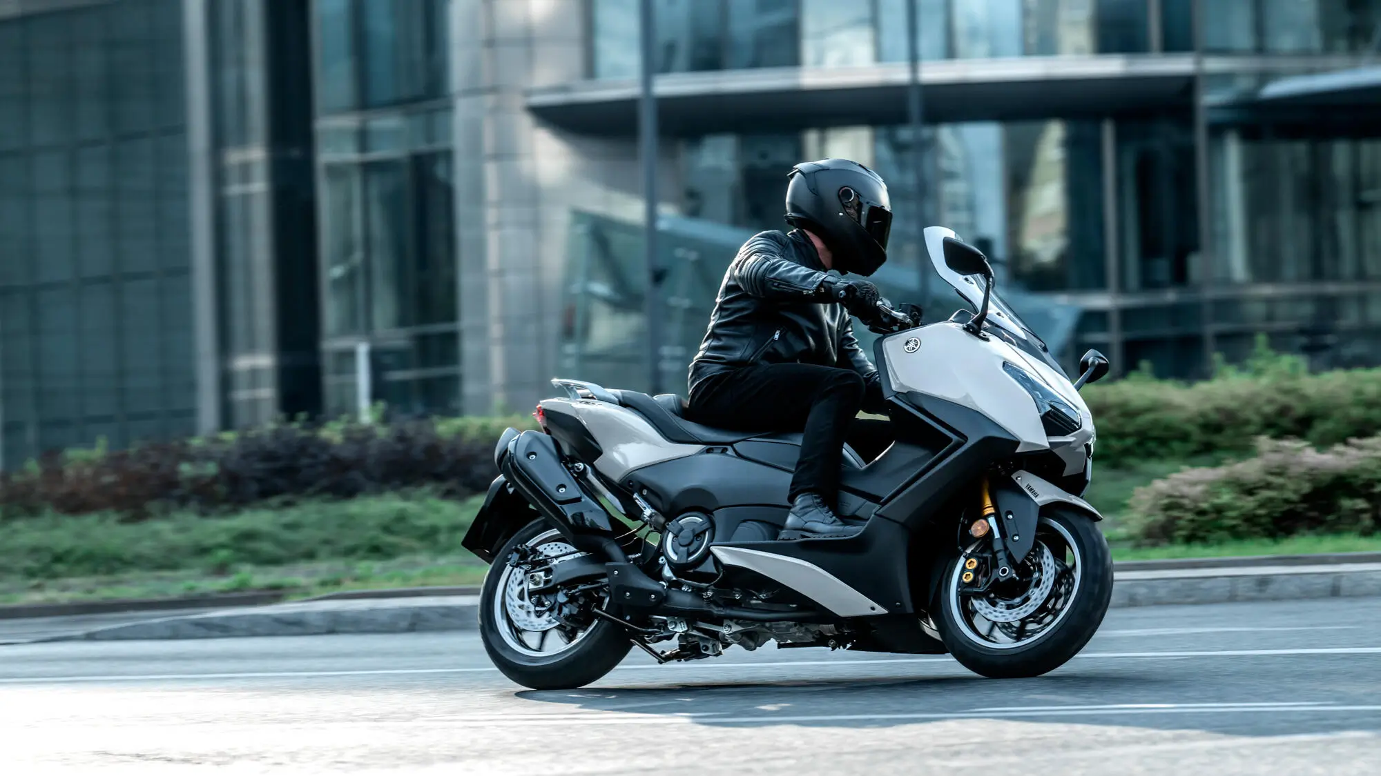 Ein Motorradfahrer auf einer 2025 Yamaha TMAX Tech MAX fährt durch eine städtische Umgebung.