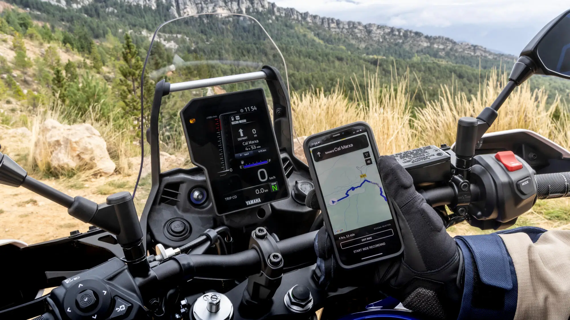 Motorradfahrer hält ein Smartphone mit Navigations-App neben dem Display einer Yamaha XTZ700.