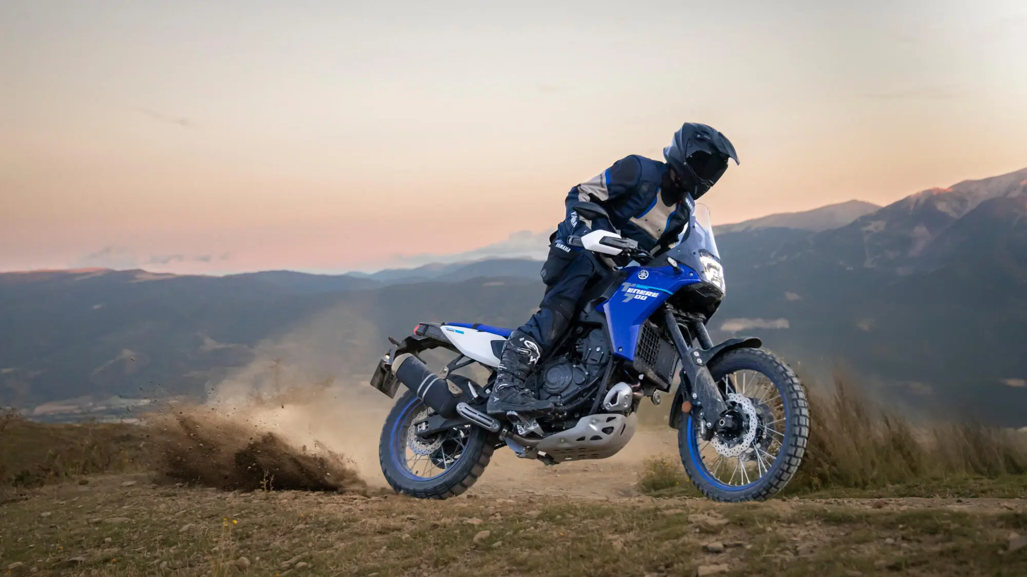 Ein Motorradfahrer fährt eine Yamaha XTZ700 auf einem staubigen Feldweg.
