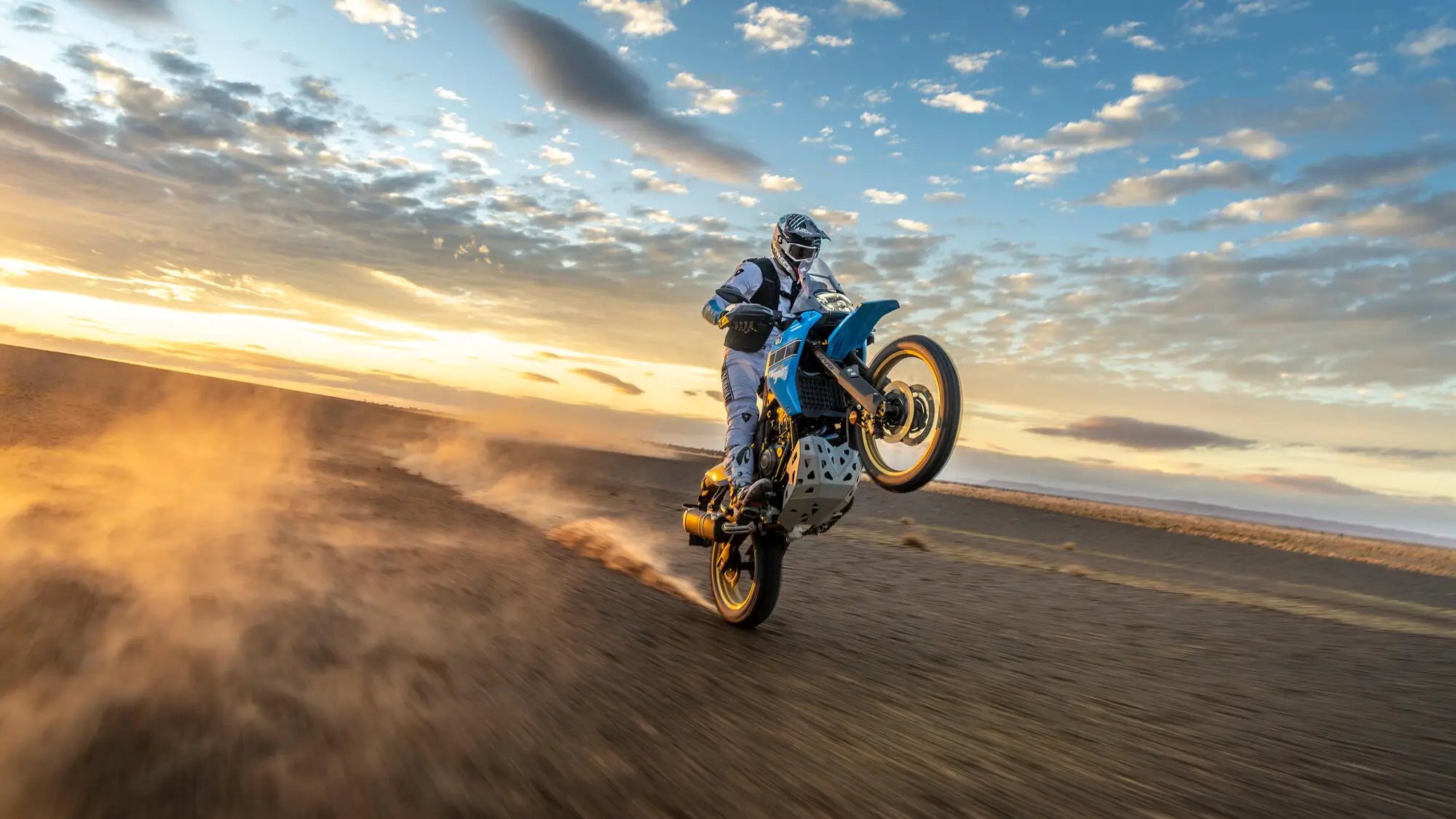Motorradfahrer macht einen Wheelie auf einer Yamaha XTZ700SPR in der Wüste bei Sonnenuntergang.
