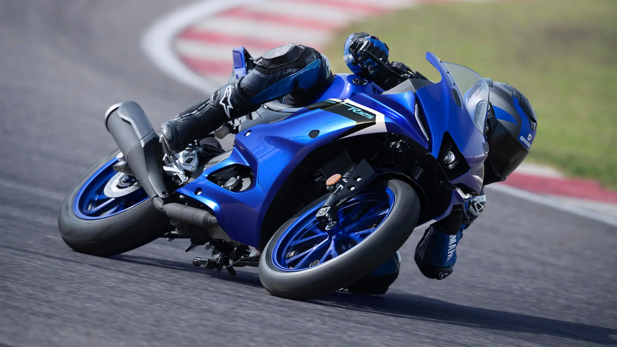 2025-Yamaha-YZF-R125-EU-Icon_Blue-Action-005-03 Ein Fahrer neigt eine blaue Yamaha YZF-R125 in einer Kurve auf einer Rennstrecke.