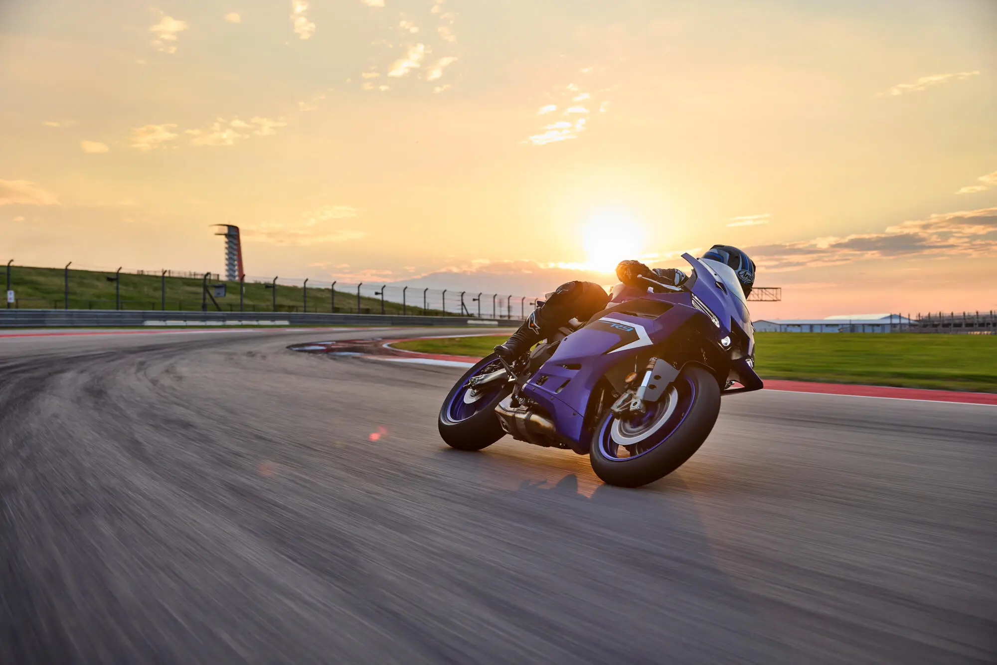 Ein Motorradfahrer fährt eine blaue Yamaha YZF900R9 bei Sonnenuntergang auf einer Rennstrecke.
