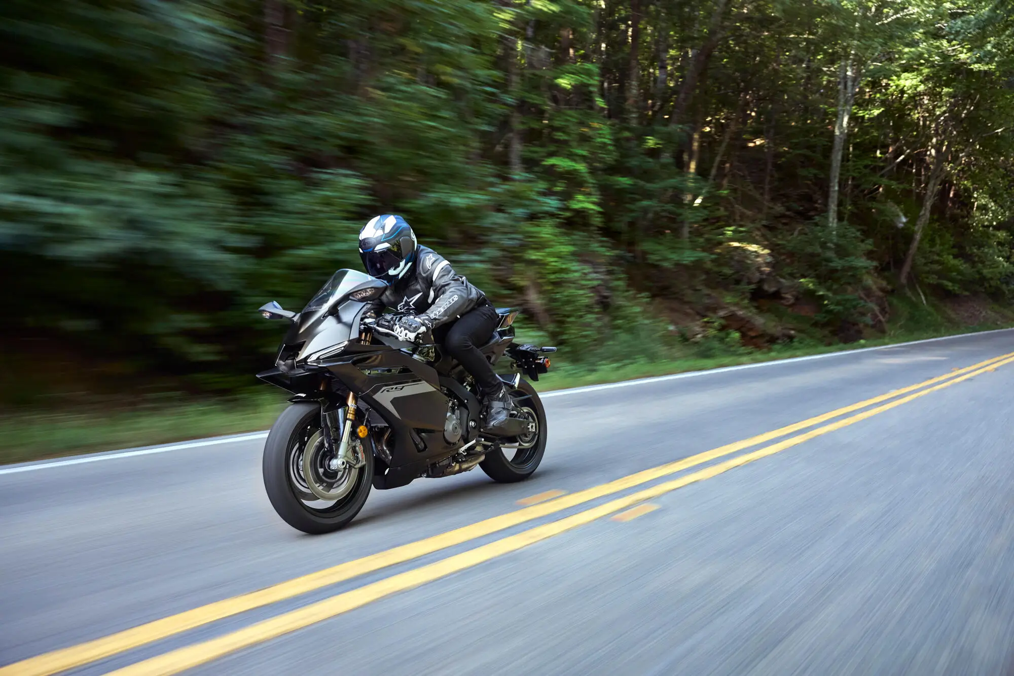 Ein Motorradfahrer fährt eine Yamaha YZF900R9 in Schwarz auf einer kurvigen Straße durch einen Wald.