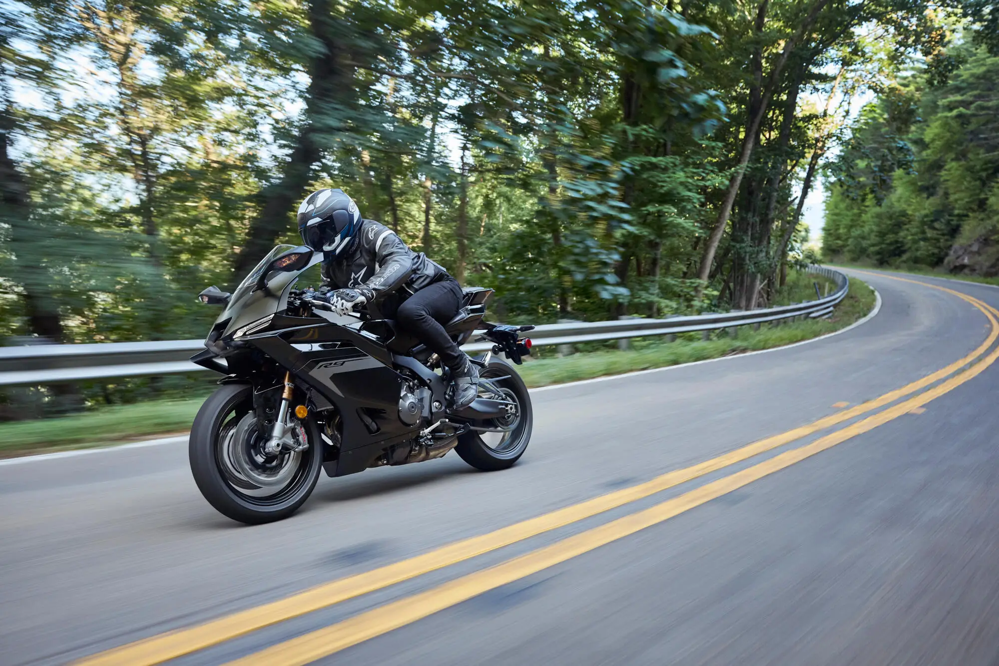 Ein Motorradfahrer fährt eine Yamaha YZF900R9 auf einer kurvigen Straße durch einen Wald.