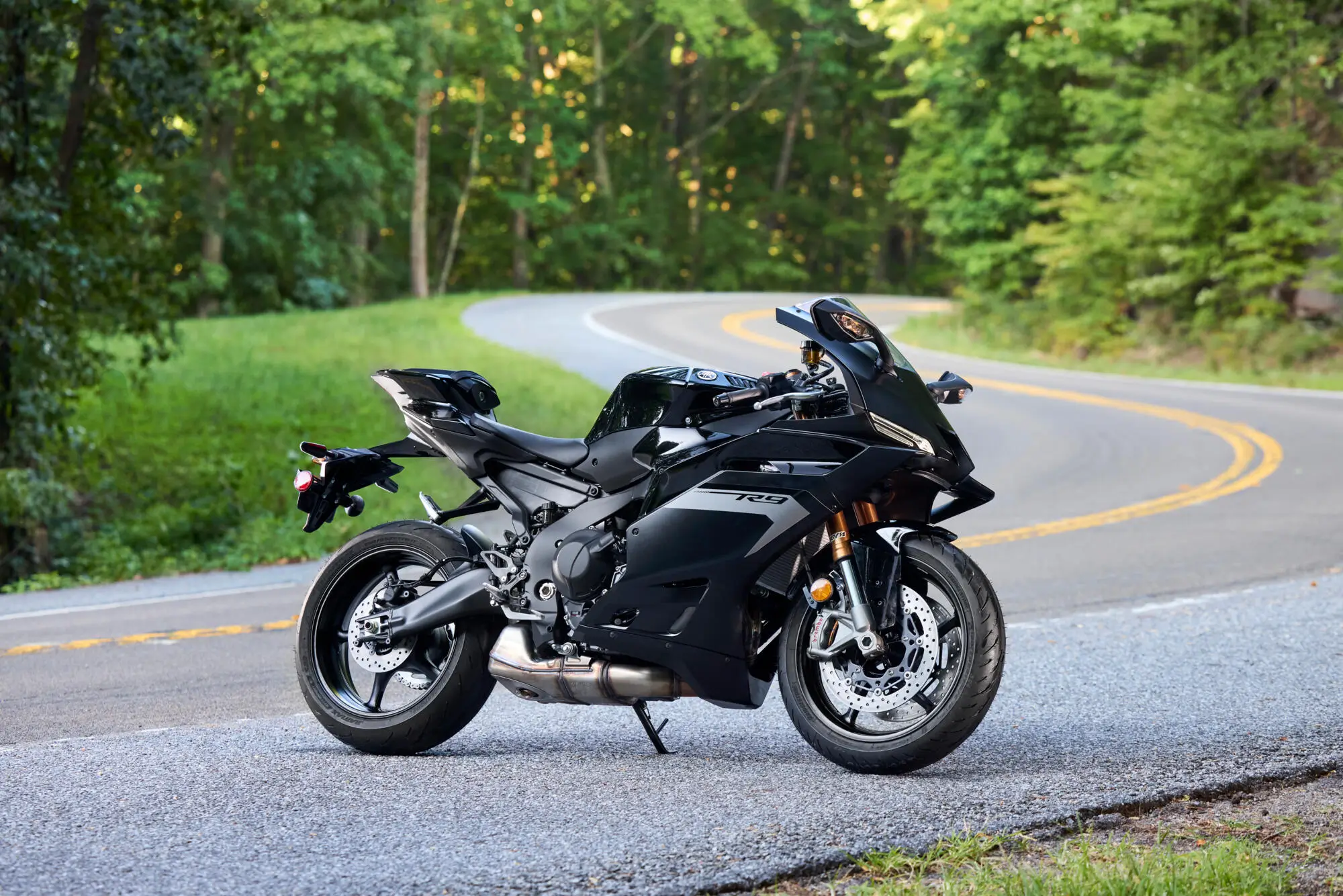 Ein Motorradfahrer fährt eine Yamaha YZF900R9 auf einer Landstraße durch einen Wald.