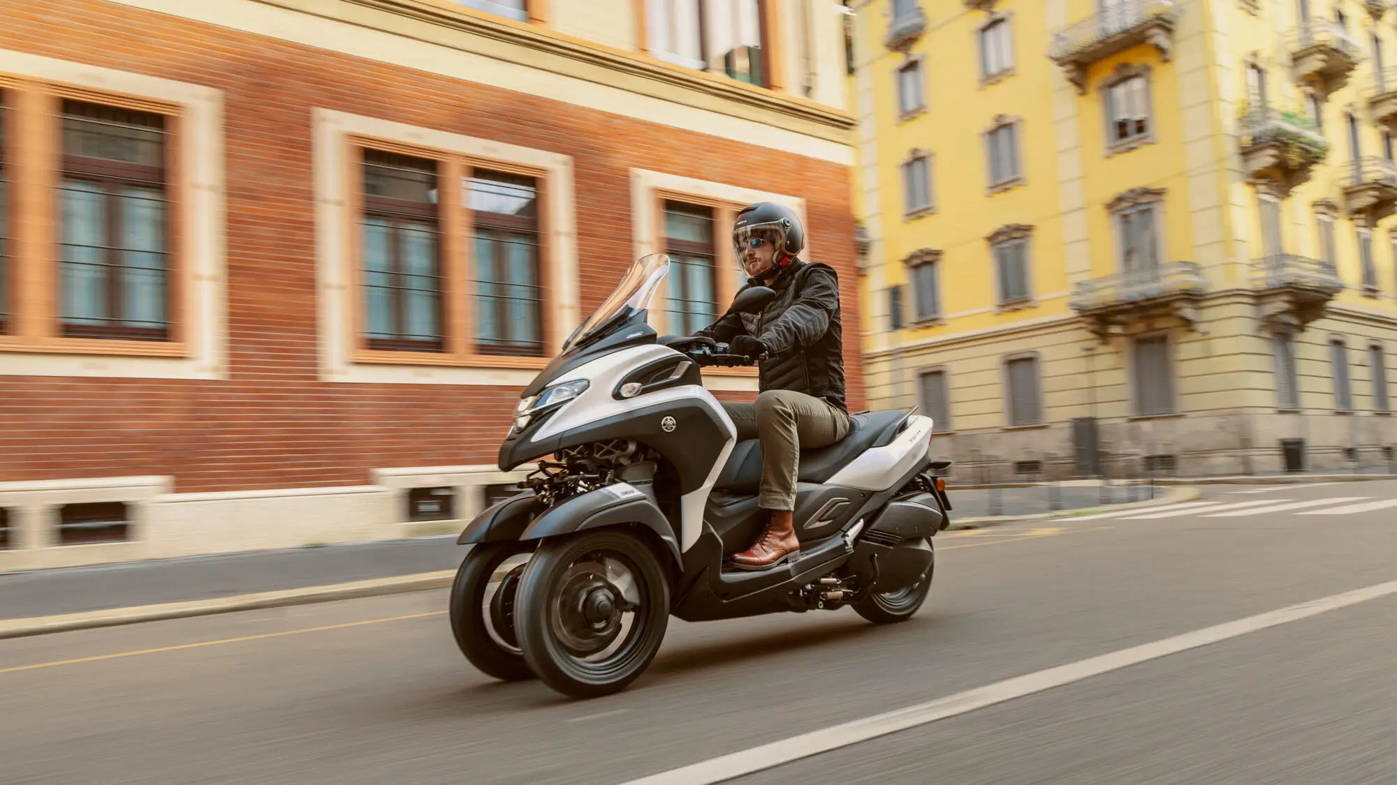 Ein Mann fährt auf einem 2025 Yamaha Tricity Roller durch eine Stadtstraße.
