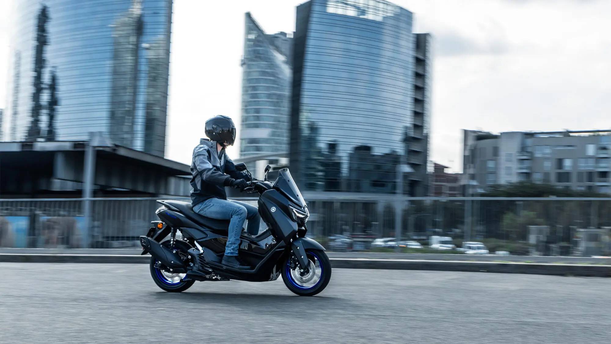 Ein Fahrer auf einem 2025 Yamaha NMAX 125 Motorrad fährt durch eine Stadtlandschaft.