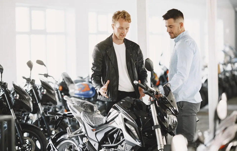AUHU Motorrad Zwei Männer betrachten gemeinsam ein schwarzes Motorrad in einem Ausstellungsraum.