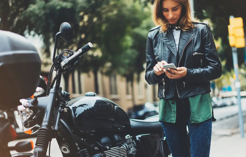 Abschleppdienst Motorrad Eine Frau in Lederjacke steht neben einem Motorrad und wählt die Nummer des Abschleppdienstes