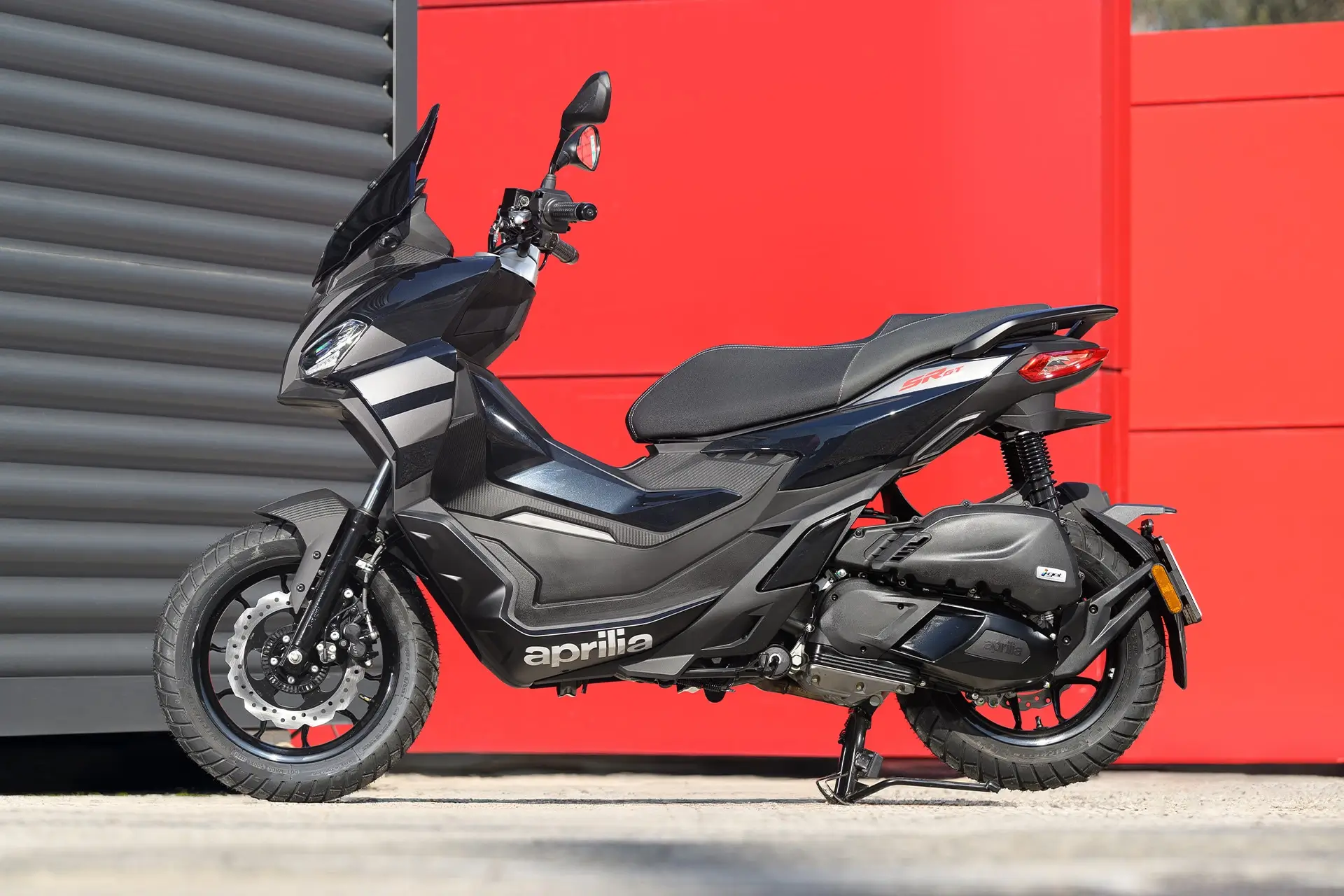Ein Aprilia SR GT 200 Motorrad steht seitlich vor einem roten Hintergrund.