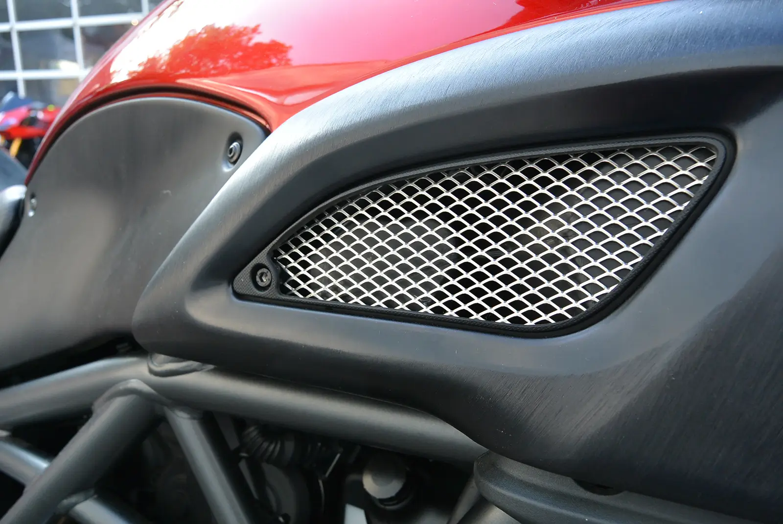 Nahaufnahme eines Motorrad-Luftgitters mit rotem Tank im Hintergrund.