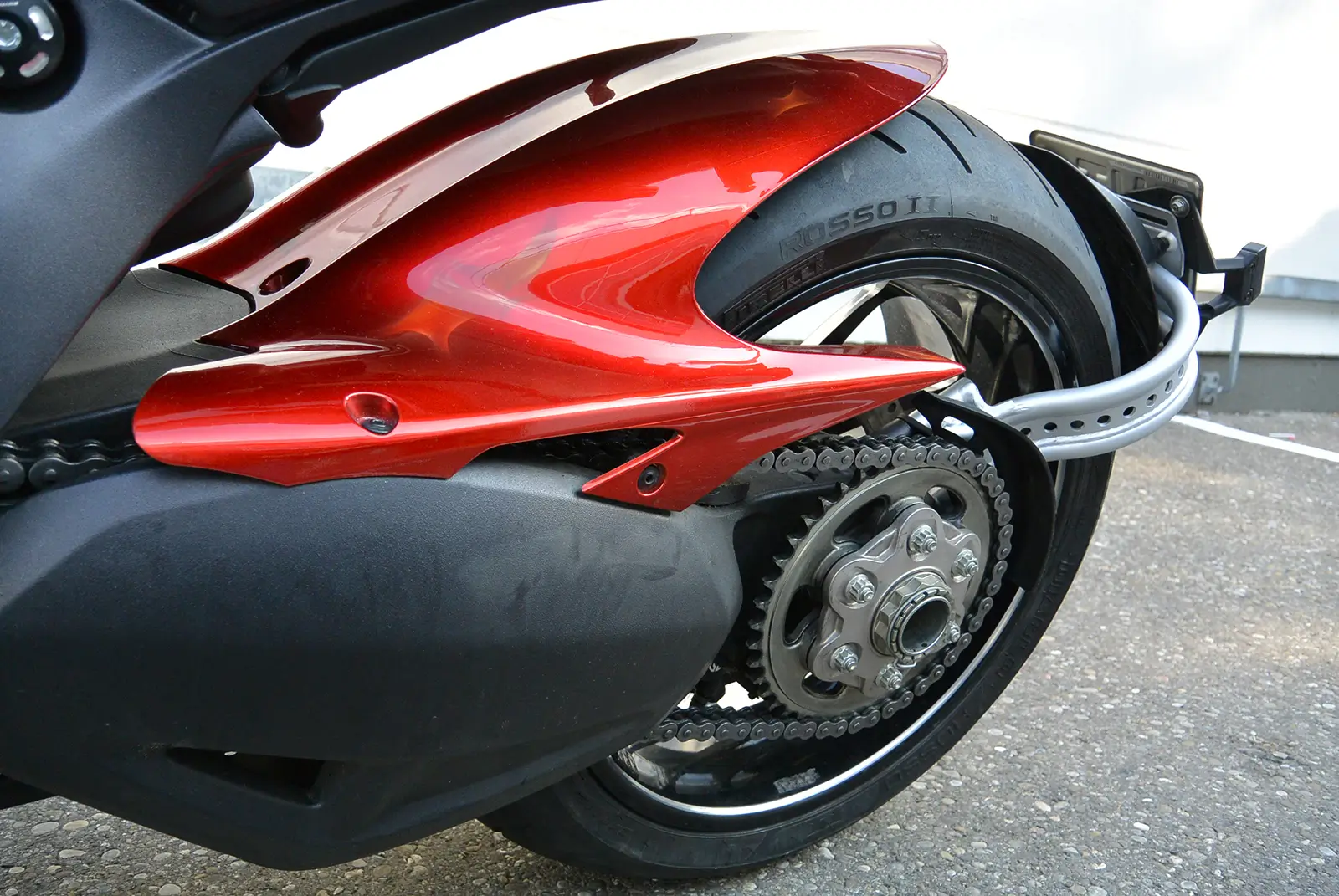 Nahaufnahme des Hinterrads eines Motorrads mit rotem Schutzblech und sichtbarer Kette.