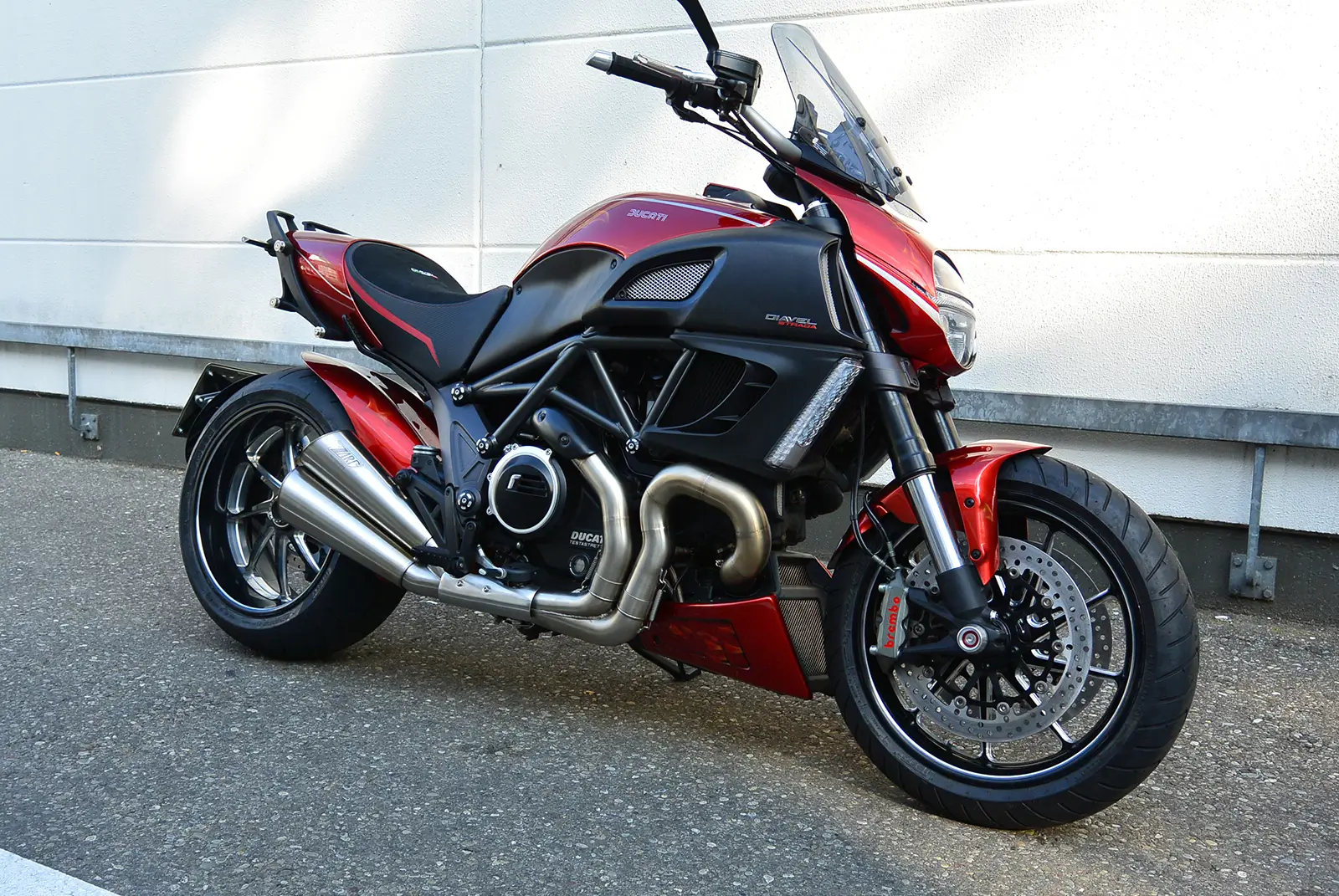 Eine rote Ducati Diavel steht auf einem Asphaltboden vor einer weißen Wand.